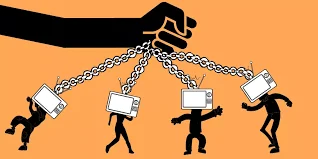 A giant hand controls chained human figures with television screens for heads