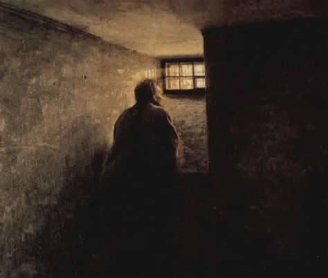 A dark painterly image of a solitary figure seen from behind, seated in a dim cell-like room with a small barred window letting in faint light.